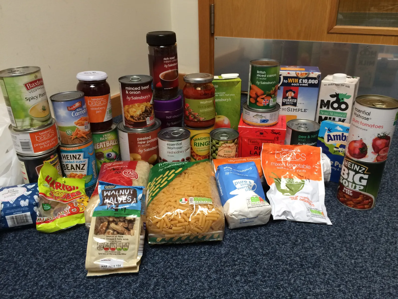 The contents of a food parcel laid out on the floor: tins of soup, meat, vegetables and fruit, pasta, rice, cereal, jam, coffee, tea, sugar, long-life milk and juice